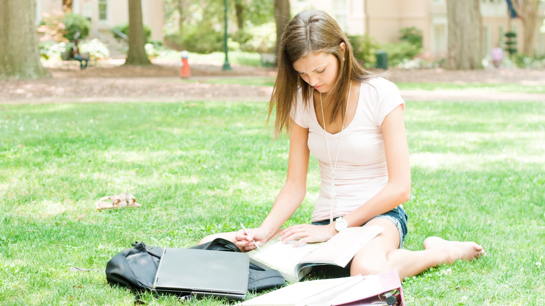 High school student reading books while sitting on grass earning college credit