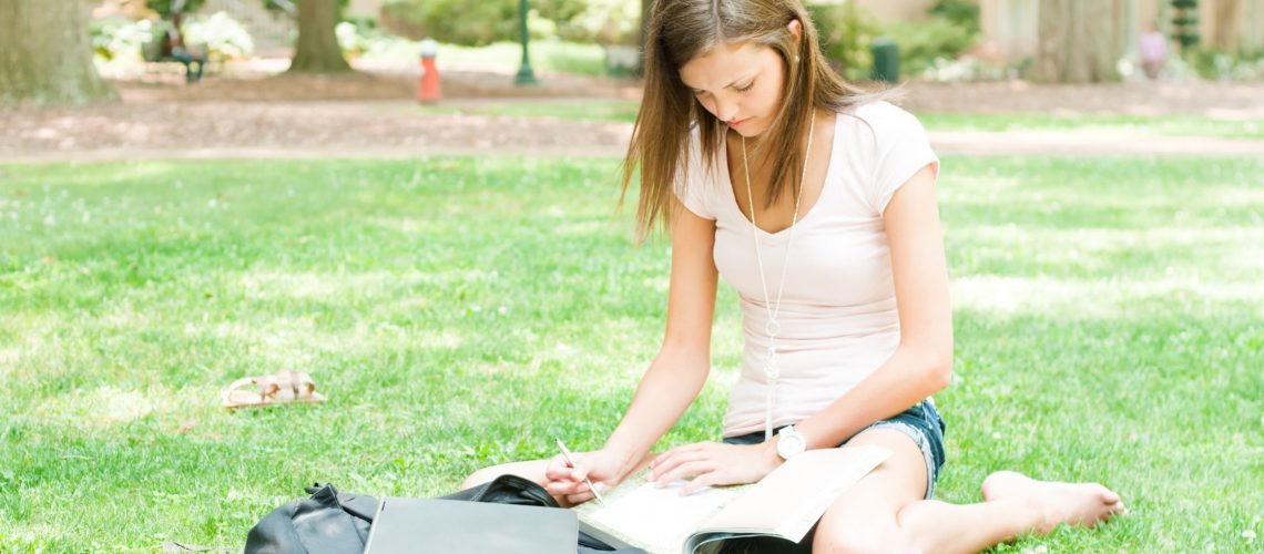 High school student reading books while sitting on grass earning college credit